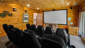 A cozy room with wooden walls, a fireplace, a projector screen, and several black chairs. - Summer Starts Here + Breathtaking Views (Pigeon Forge)