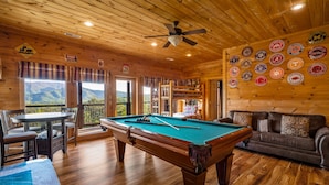 A wooden interior with a pool table, a sofa, and a wall decorated with various college logos. - Summer Starts Here + Breathtaking Views (Pigeon Forge)
