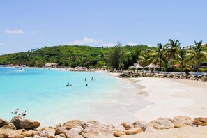 A beach with clear turquoise water, rocky shoreline, and palm trees. - Romantic Antigua Getaway – Oceanfront Condo with Resort Amenities (St. John's)