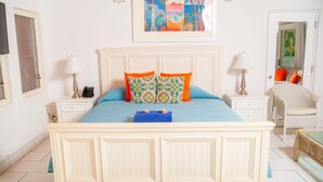 A bedroom with a large bed, two nightstands, a chair, and a painting on the wall. - Romantic Antigua Getaway – Oceanfront Condo with Resort Amenities (St. John's)