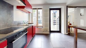 A modern kitchen with a red accent wall, a built-in oven, and a window overlooking the street. - Roesselmann 2bdrm 1 Parking (Colmar)