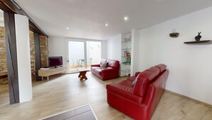 A spacious living room with a red leather sofa, a television on a white cabinet, and a dining area with a table and chairs. - Roesselmann 2bdrm 1 Parking (Colmar)