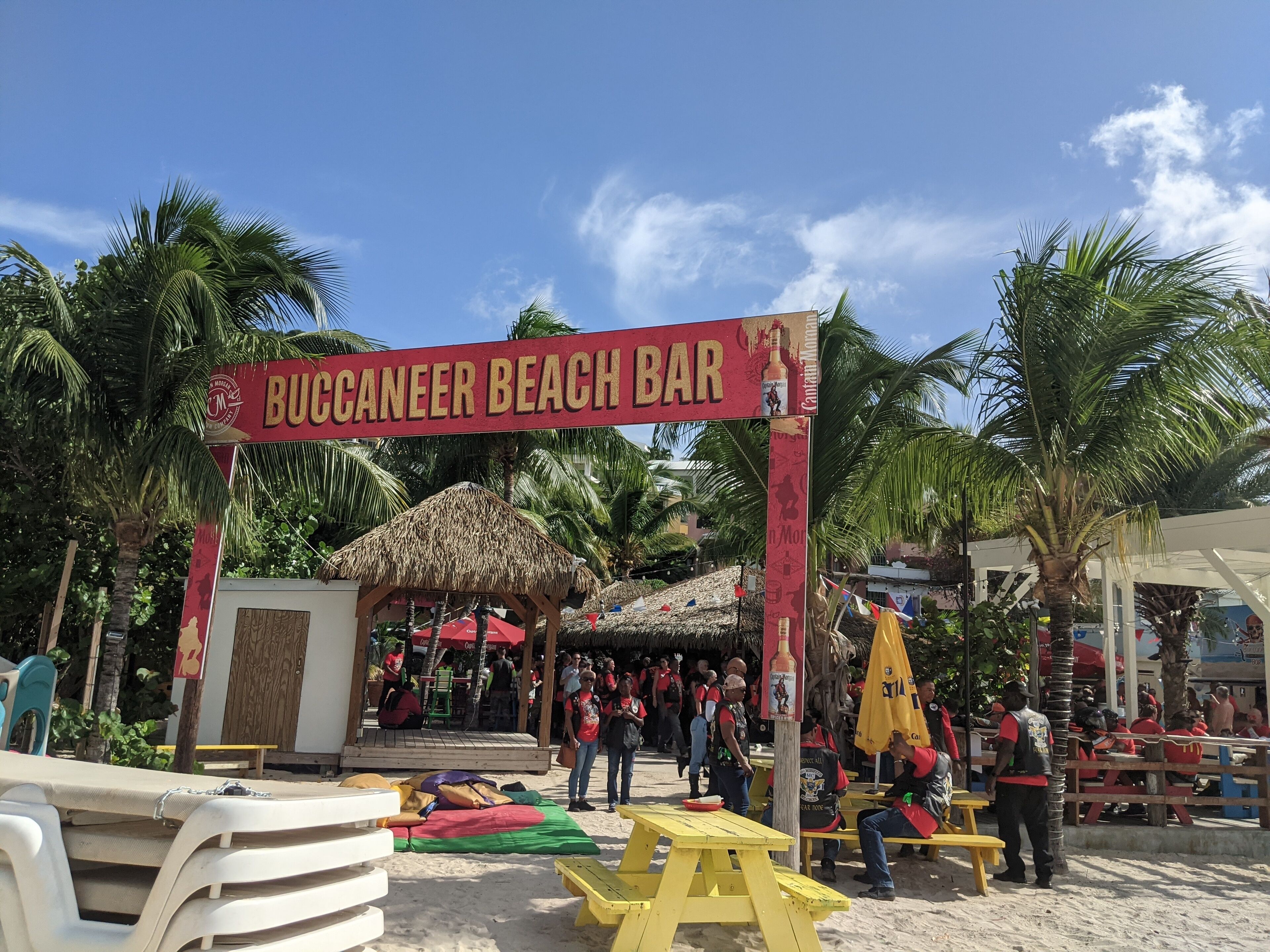 A beach bar with a thatched-roof structure, outdoor seating, and palm trees.