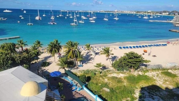 A beach with a pool area, palm trees, and boats in the water. - Large Pool/ 1 BR/1Bath  Apt. in Beautiful St. Martin in Simpson Bay! (Simpson Bay)