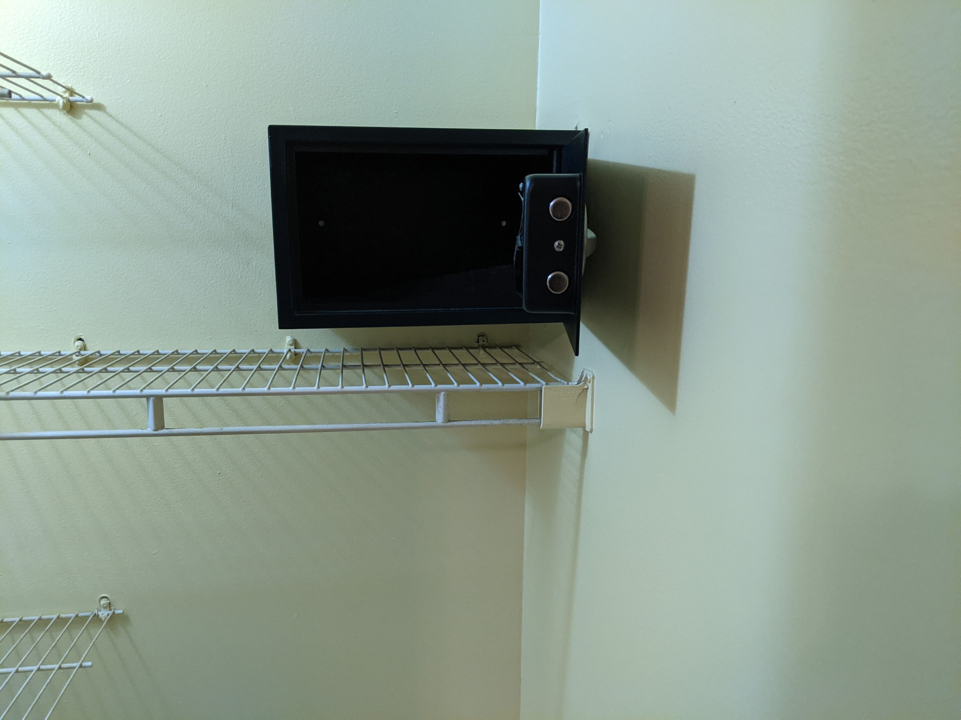A microwave oven mounted on a wall with a metal rack below it.