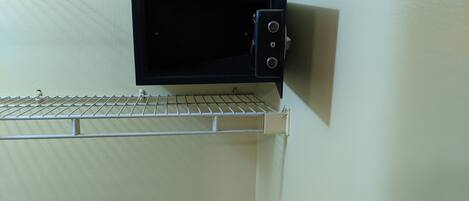 A microwave oven mounted on a wall with a metal rack below it.