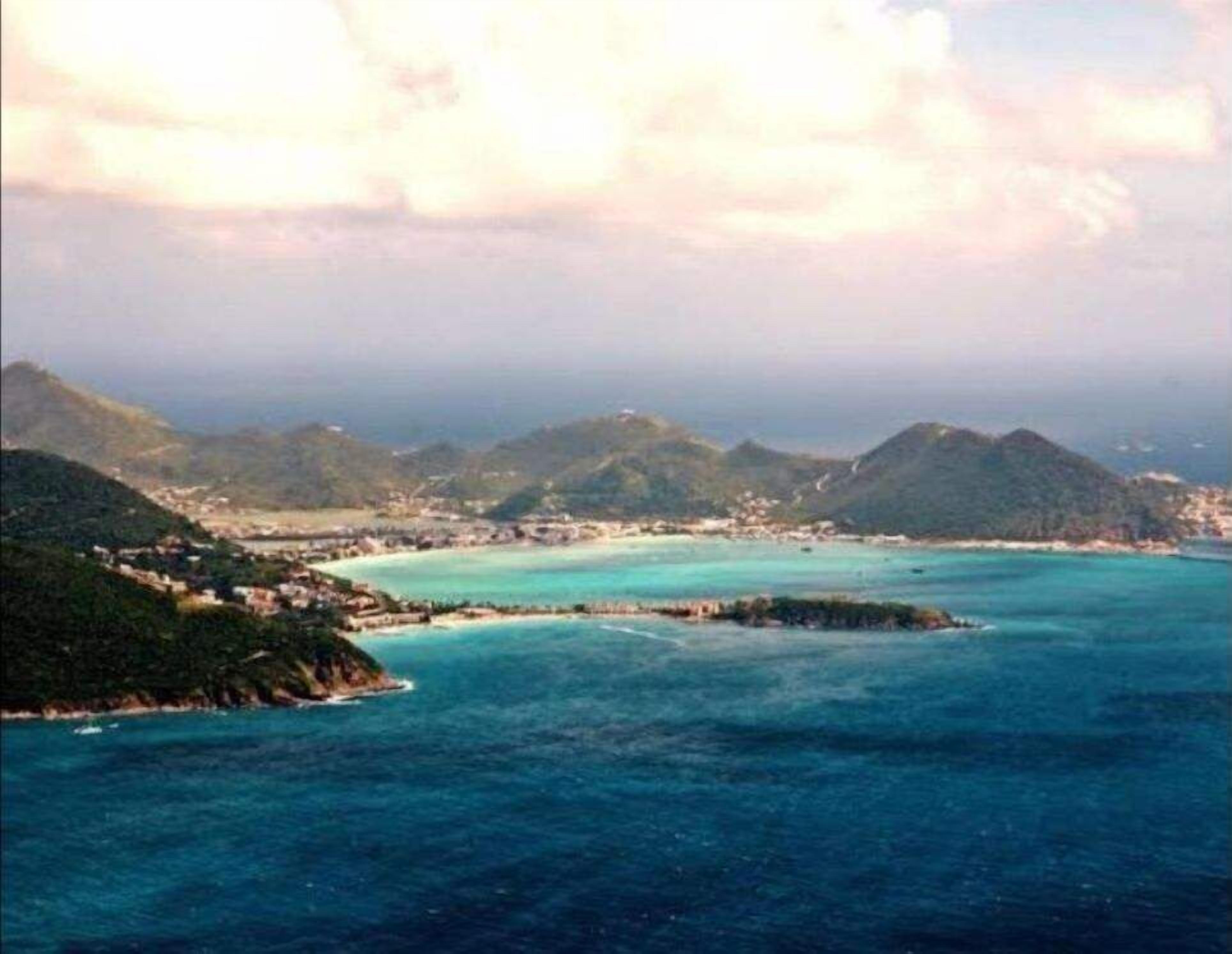 Un paysage côtier avec une petite île, des eaux turquoise et limpides, et une ville située sur le continent.
