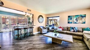A spacious living room with a wooden floor, a sofa with cushions, a coffee table, and a bar area with stools. - VEGAS Garden Oasis (Las Vegas)