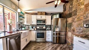 A modern kitchen with stainless steel appliances, wooden flooring, and a stone accent wall. - VEGAS Garden Oasis (Las Vegas)