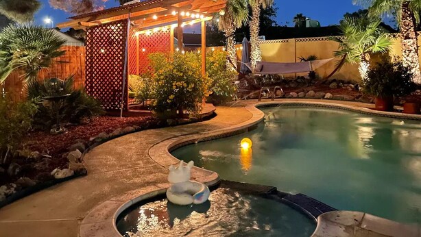 A nighttime pool area with a hot tub, a wooden pergola with string lights, and a palm tree. - VEGAS Garden Oasis (Las Vegas)