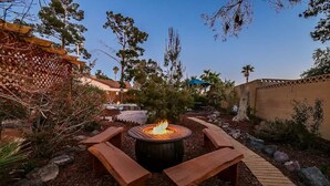A circular fire pit with benches around it, surrounded by a garden with trees and a wooden deck. - VEGAS Garden Oasis (Las Vegas)