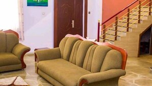 A living room with a sofa and armchairs, a staircase with a red railing, and a door in the background. - Whyte View Lodge (Sekondi-Takoradi)