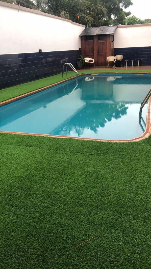 A rectangular swimming pool with a metal ladder, surrounded by artificial grass. - Whyte View Lodge (Sekondi-Takoradi)