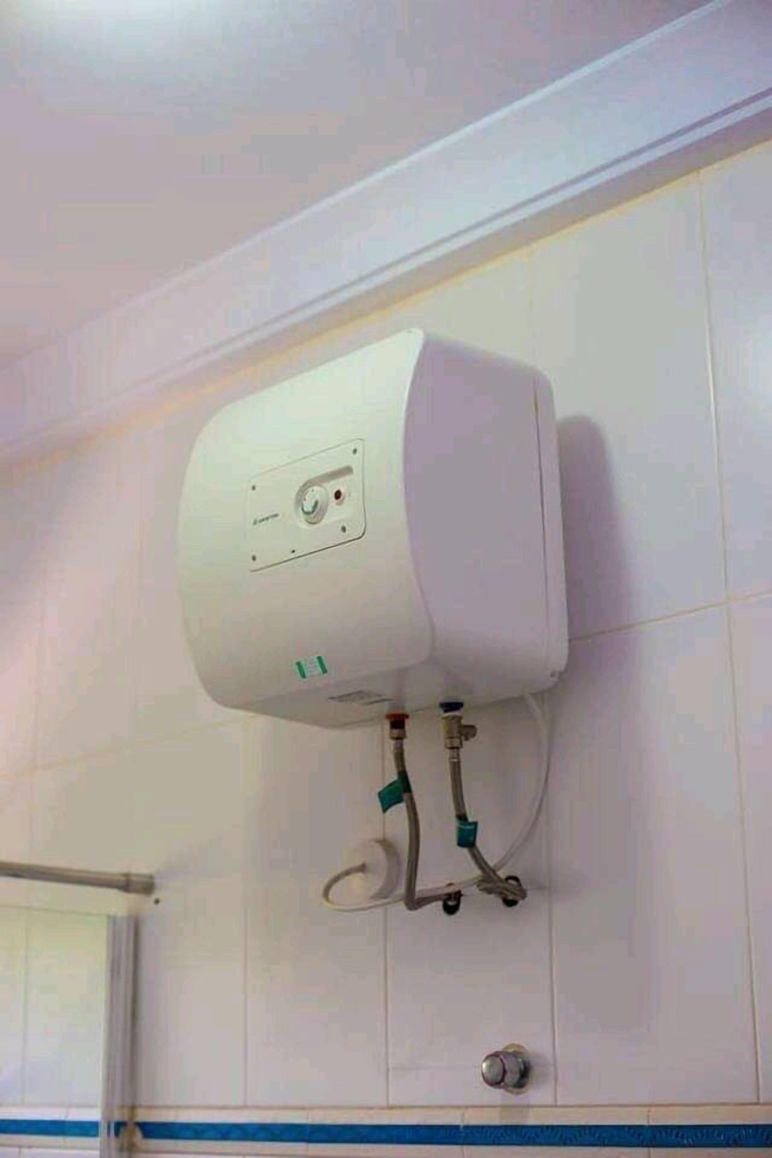 Calentador de agua blanco instalado en una pared con azulejos y una franja azul.