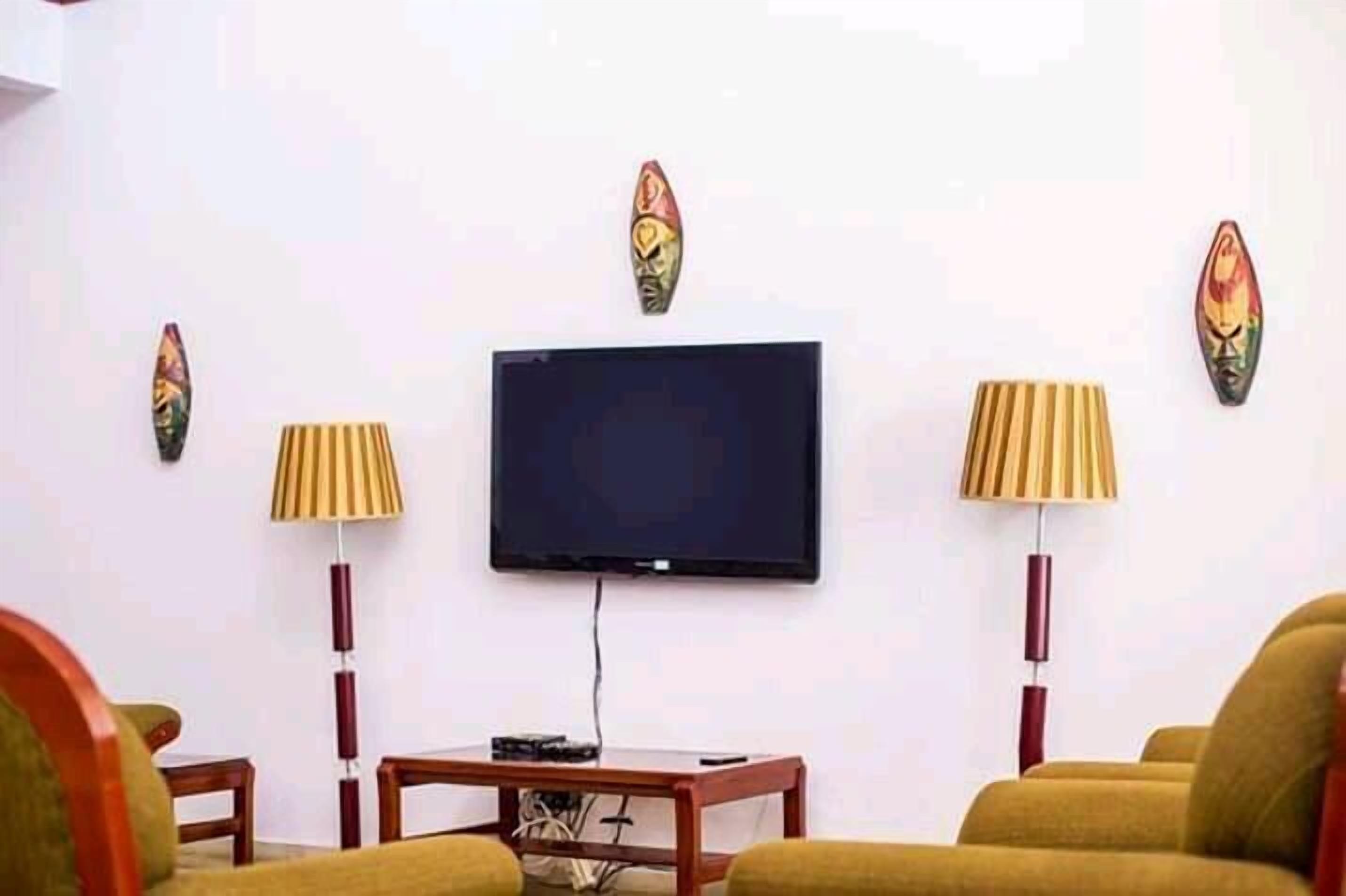 A living room with a flat-screen TV mounted on the wall, two floor lamps, and a small table.