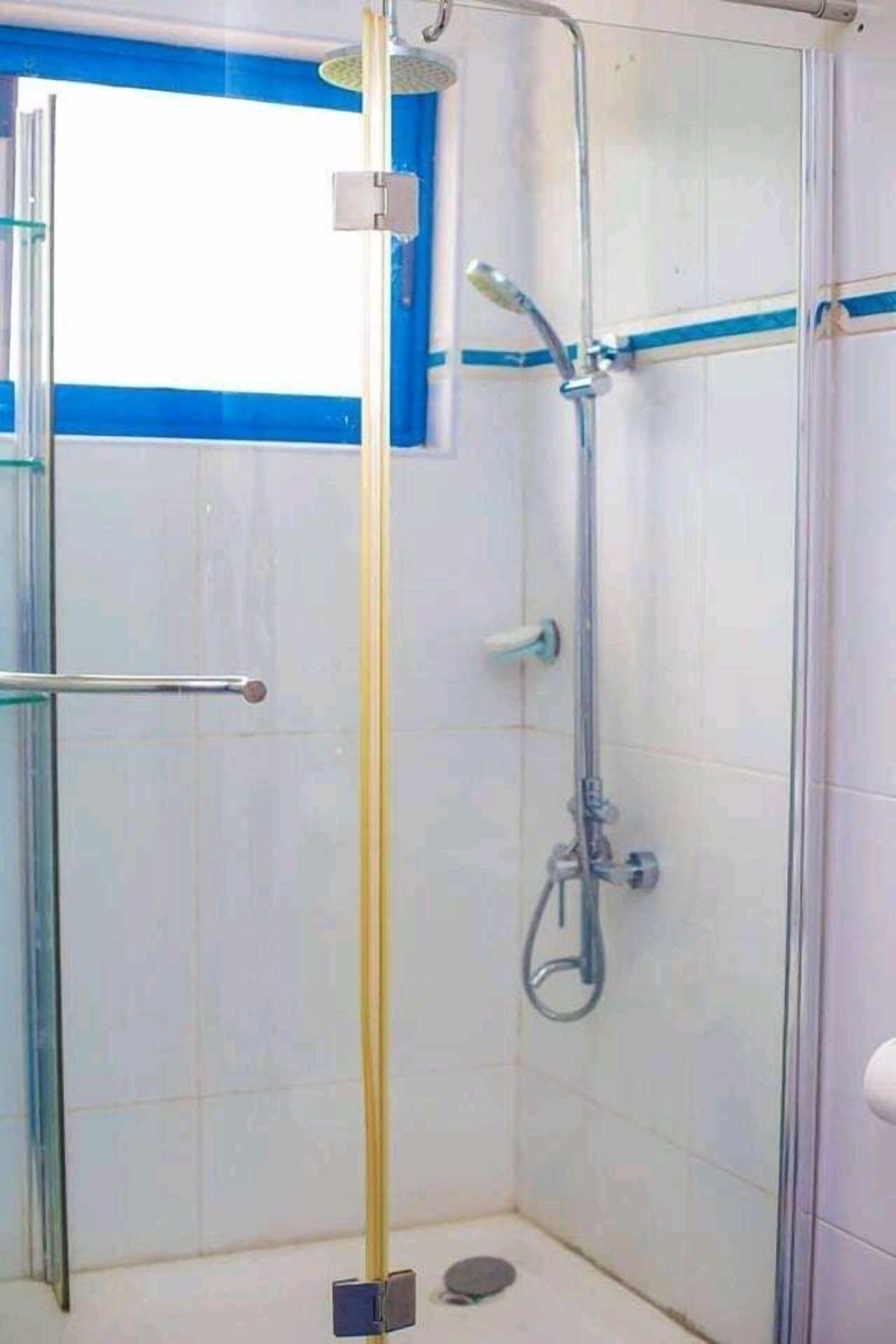 A small, enclosed shower area with a glass door, a showerhead, and a handheld shower attachment.