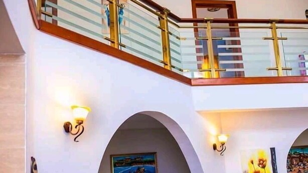 A multi-level interior with a glass railing, arched doorways, and wall-mounted lighting. - Whyte View Lodge (Sekondi-Takoradi)