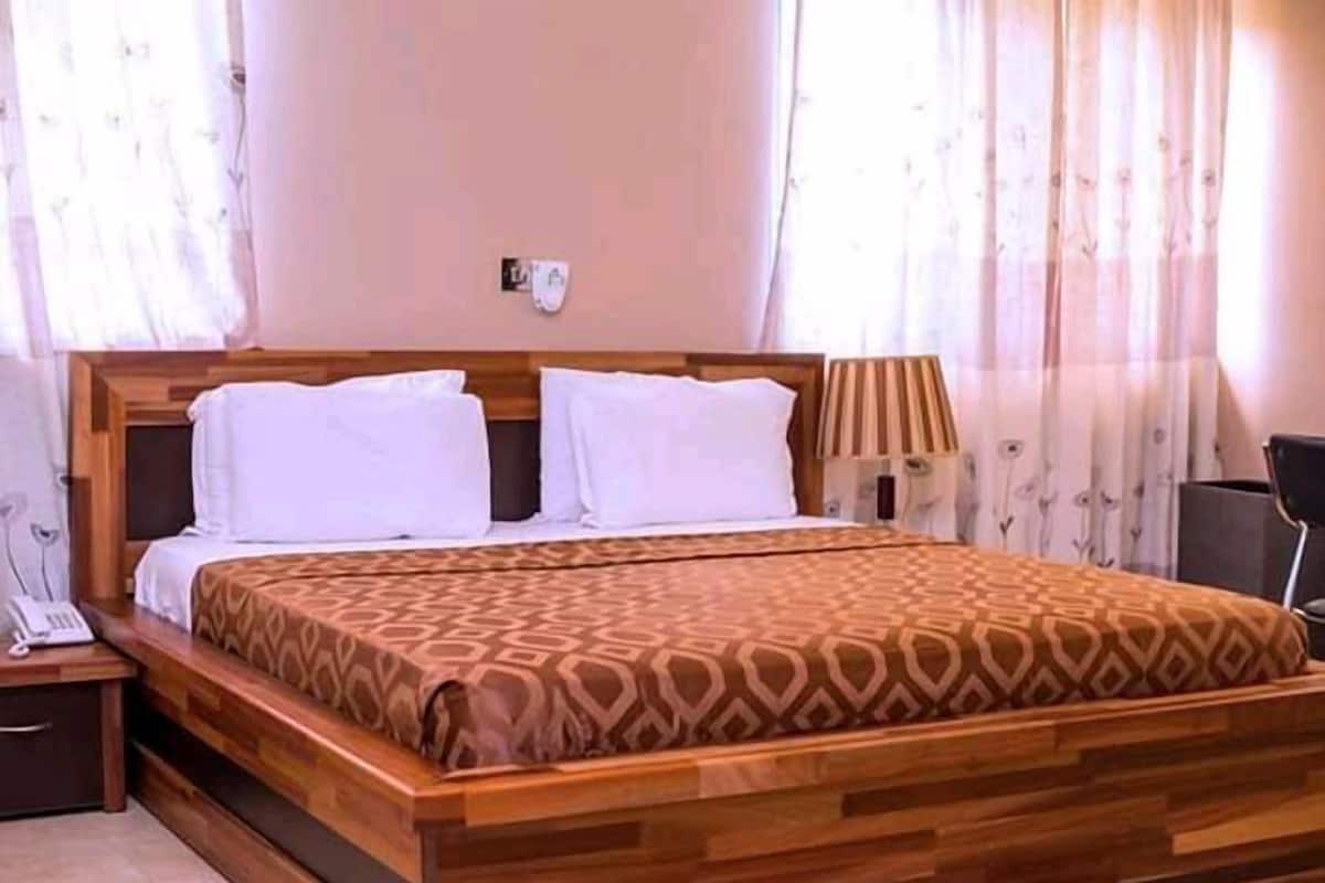 A neatly made bed with a patterned bedspread, a bedside table with a lamp, and a wall-mounted telephone.