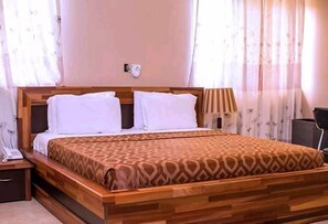 A neatly made bed with a patterned bedspread, a bedside table with a lamp, and a wall-mounted telephone. - Whyte View Lodge (Sekondi-Takoradi)