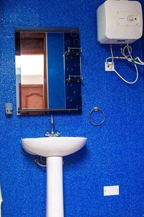 A bathroom with a blue tiled wall, a white sink, a mirror, and a white water heater. - Whyte View Lodge (Sekondi-Takoradi)