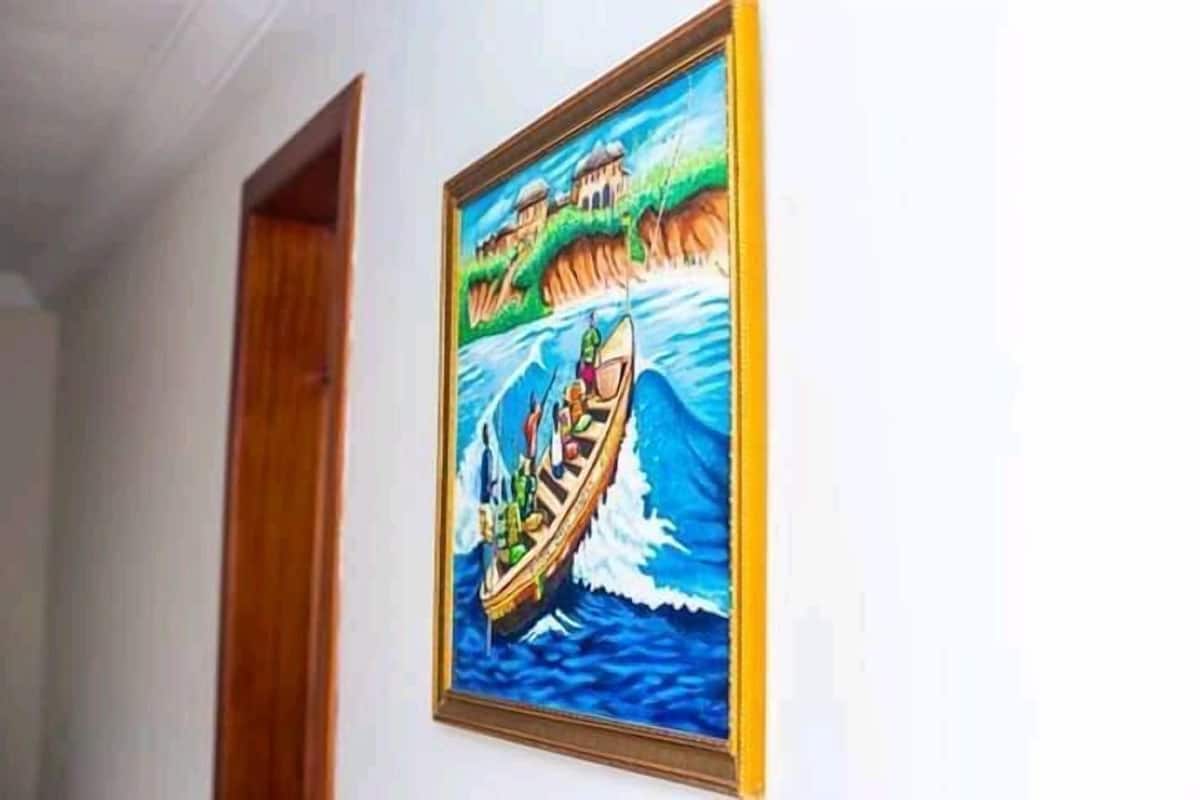A framed painting of a boat on water with buildings in the background.