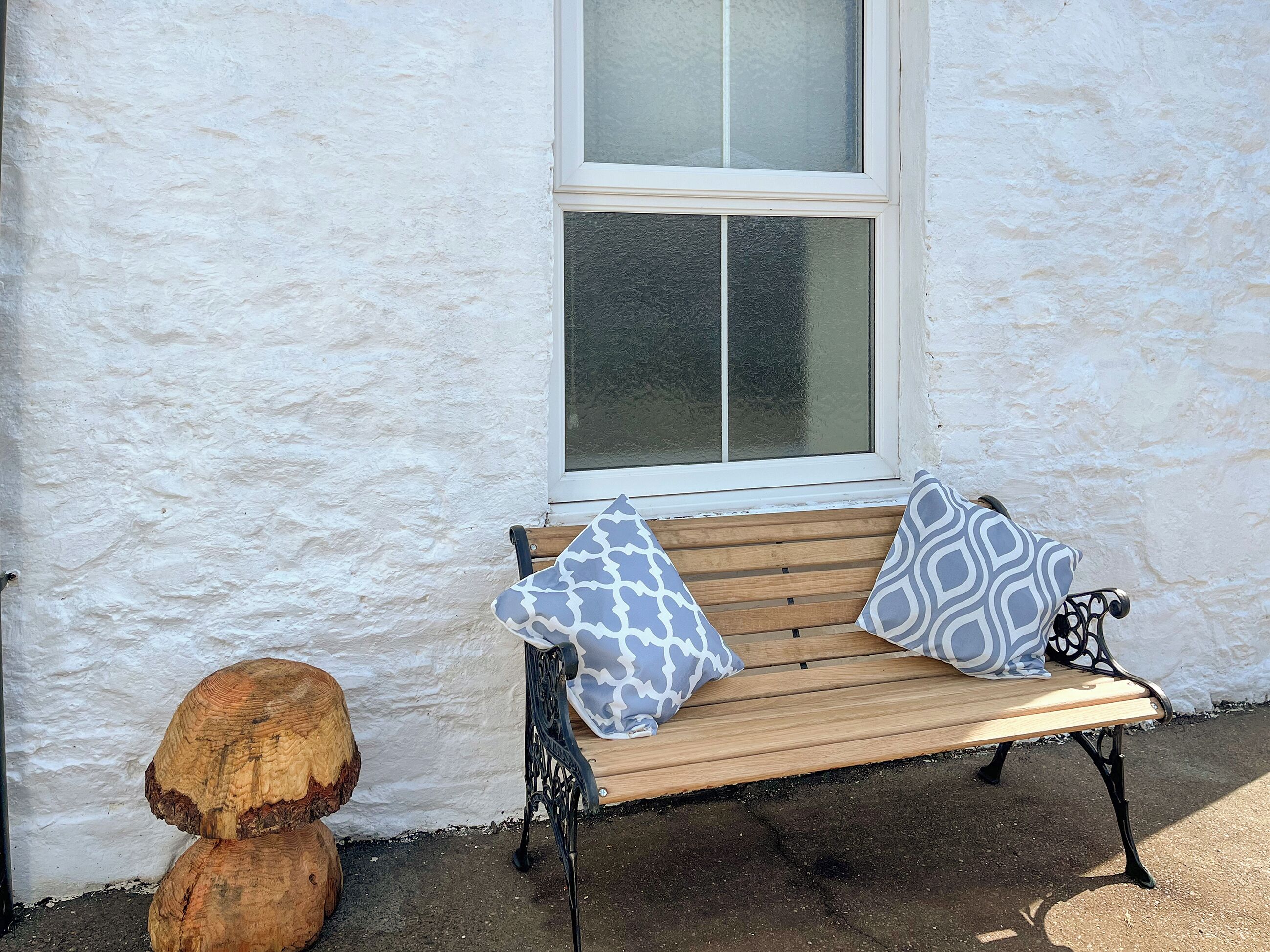 A wooden bench with patterned cushions against a white wall, next to a window with frosted glass.