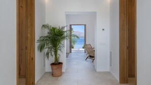 A hallway with a potted plant, wooden doors, and a view of the sea. - VILLA ES BARCARES (Alcúdia)