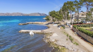 A coastal property with a clear view of the sea, a rocky shoreline, and a pathway leading to a building with multiple balconies. - VILLA ES BARCARES (Alcúdia)