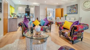 Un salon moderne avec deux canapés colorés, une table basse en verre et un coin repas comprenant une table et des chaises blanches.