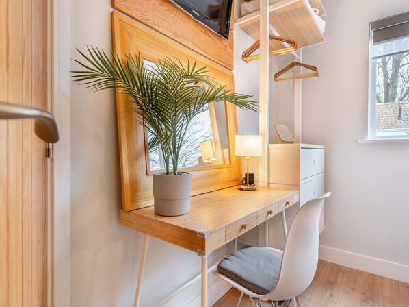 A modern bathroom with a wooden vanity, a mirror, a potted plant, a white chair, and a window with a view of trees.