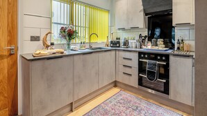 Une cuisine moderne avec des meubles gris, un four encastré et une fenêtre avec des stores jaunes.