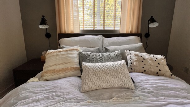 Una cama con muchas almohadas y una ventana con cortinas.