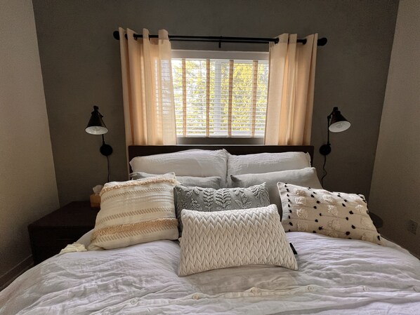 A bed with multiple pillows and a window with curtains. - 900 square foot Studio loft in Fairhaven (Bellingham)