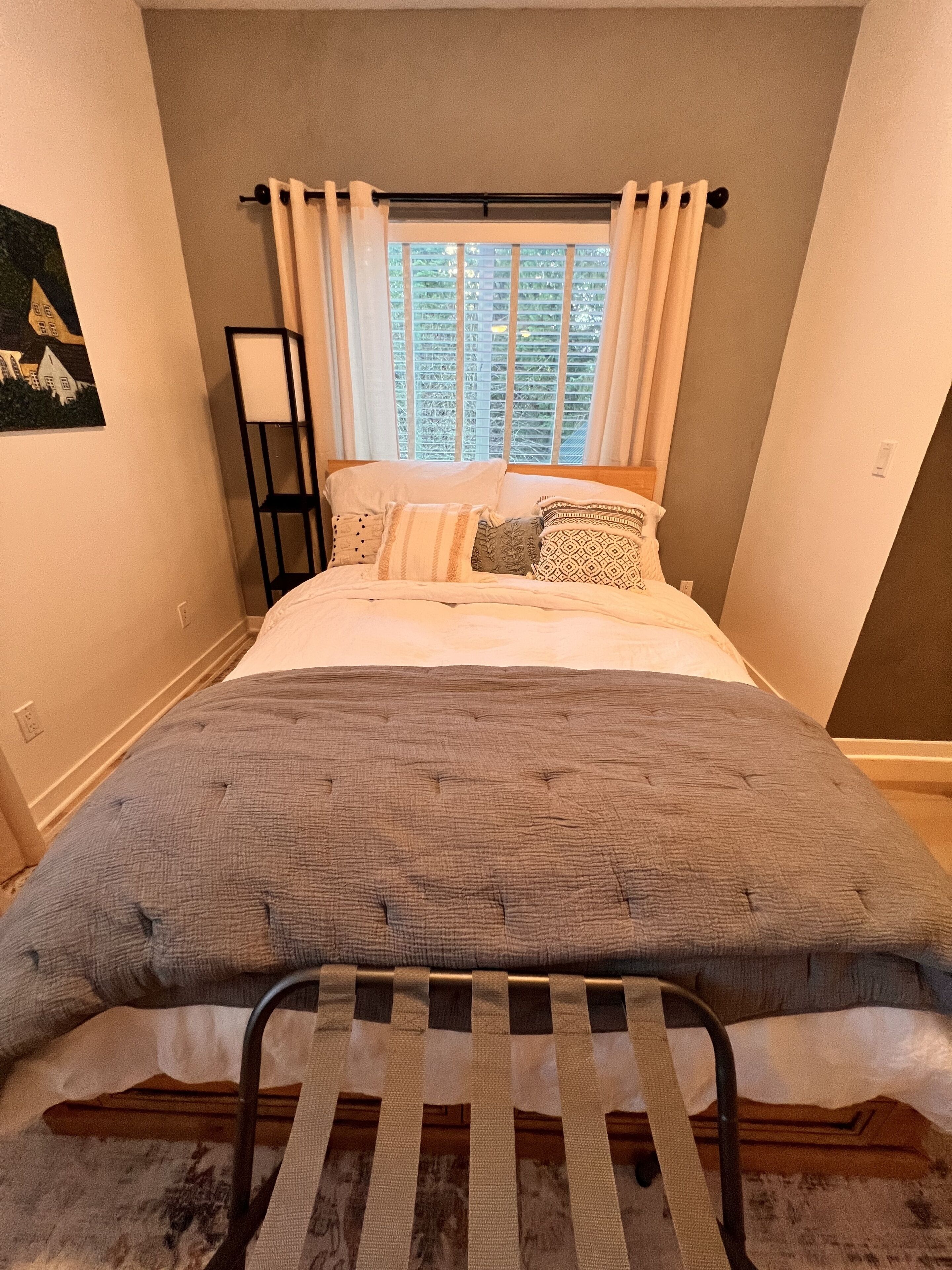 Un dormitorio con cama, ventana con cortinas, mesita de noche y estante en la pared.