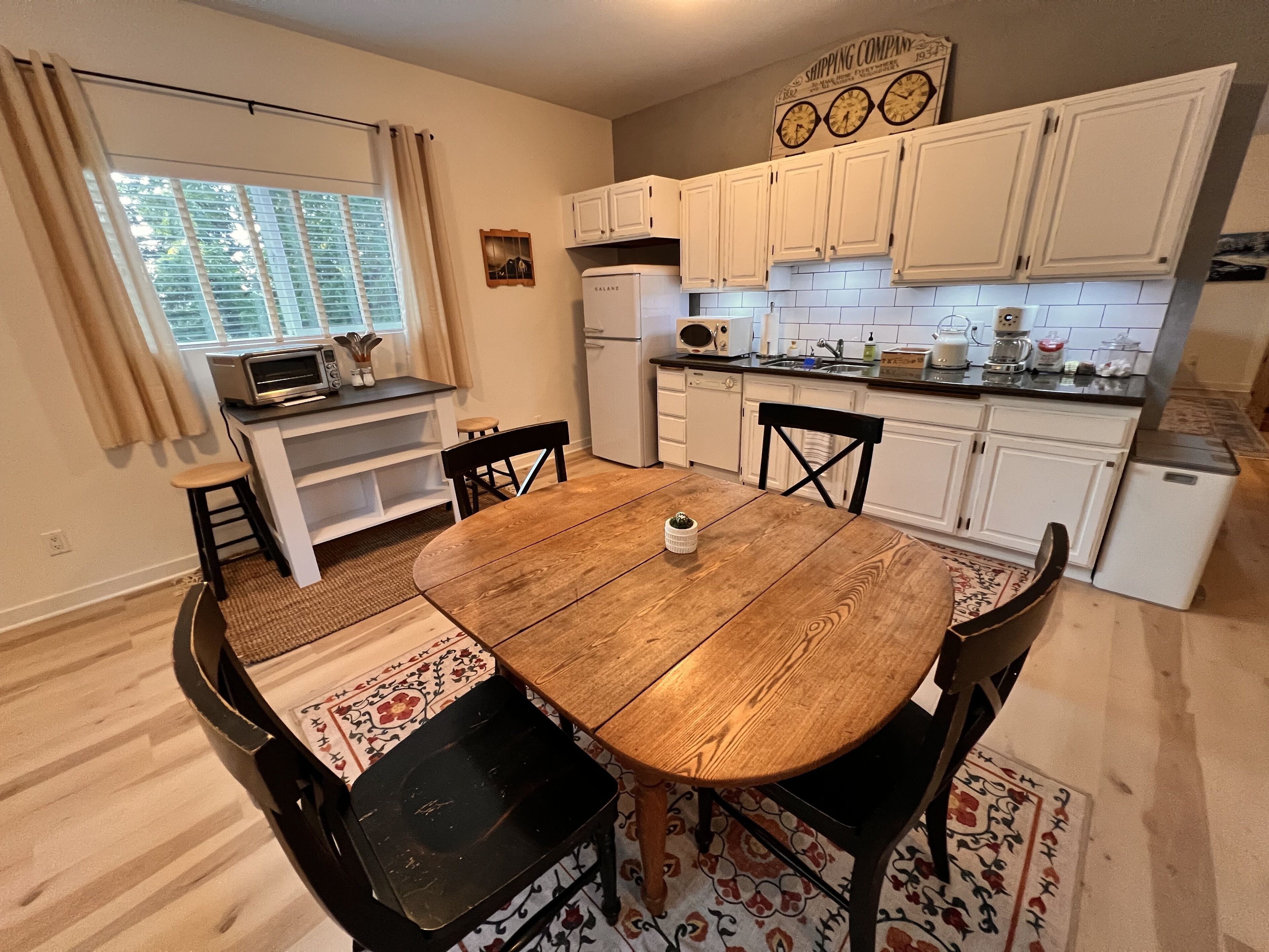 A compact kitchen with white cabinets, a dining table, and a small refrigerator.