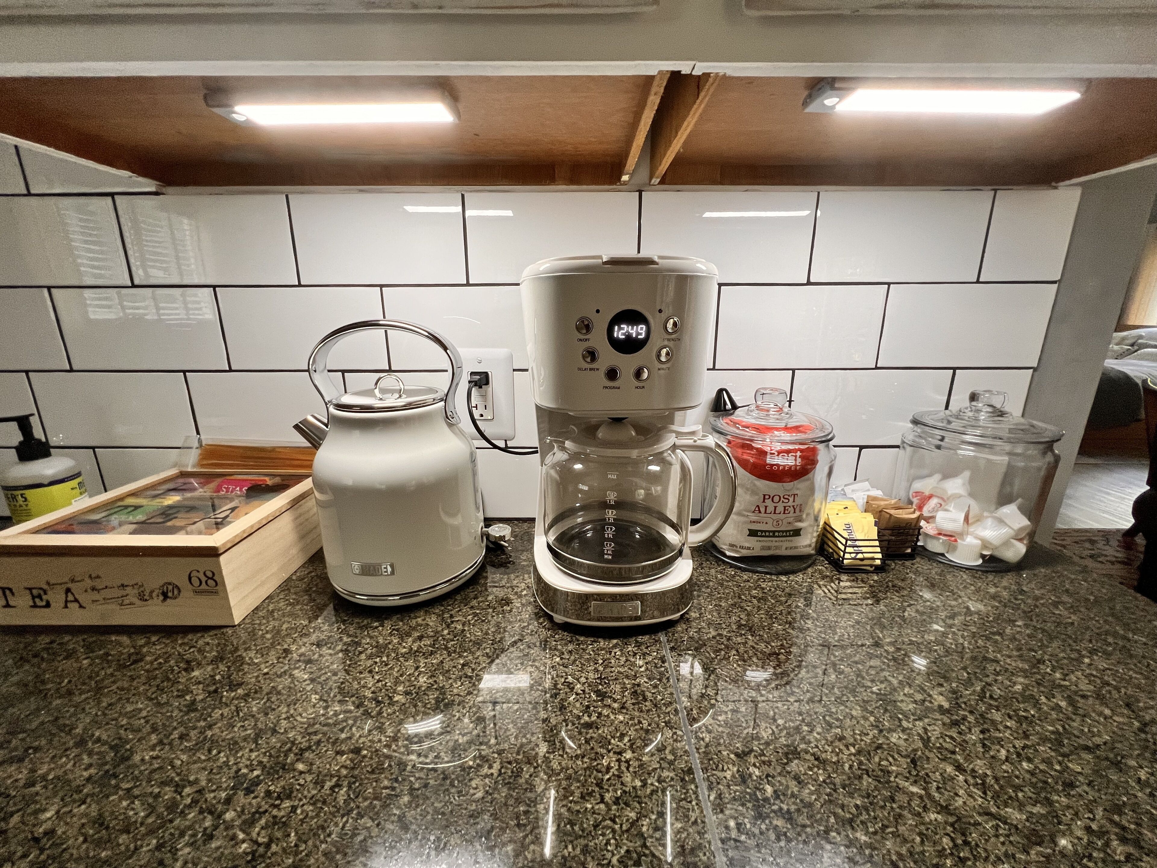 A kitchen with a coffee maker, kettle, and various containers on the counter.