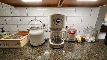 A kitchen with a coffee maker, kettle, and various containers on the counter.