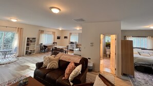 Amplia sala de estar con sofá, mesa de comedor y estantería. Se ve un dormitorio separado a través de una puerta abierta.