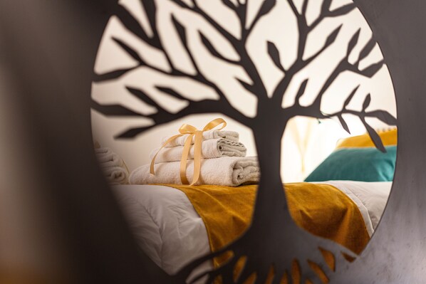 A bed with neatly folded towels and a yellow blanket, viewed through a circular cutout with a tree silhouette. - Apartment in the center of Palermo (Palermo)