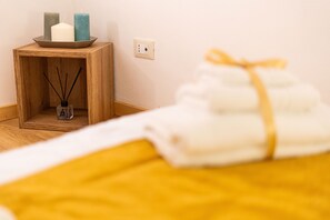 A neatly arranged bathroom with a wooden side table holding candles and a reed diffuser, a towel rack with folded towels, and a visible electrical outlet on the wall. - Apartment in the center of Palermo (Palermo)