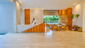 Um hall de hotel moderno com balcão de recepção, área de estar e vista para o exterior com vegetação.