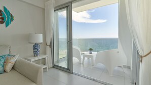 Varanda com vista para o mar, um sofá branco, uma mesa pequena com abajur e um objeto decorativo na parede.