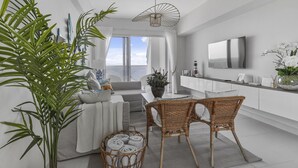 Uma sala de estar moderna com sofá, mesa de jantar, cadeiras de vime, uma grande planta em vaso e vista pela janela.