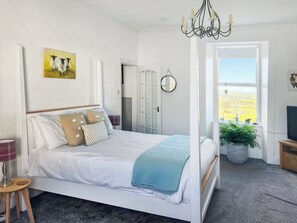 Un dormitorio con cama, candelabro, pintura, espejo y vista al exterior.