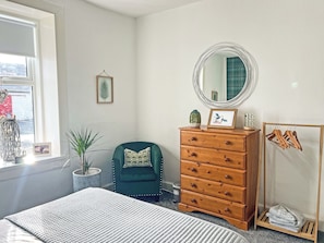 A bedroom with a bed, dresser, chair, mirror, and a window with a view. - Muirston Farmhouse - UK44977 (Cumnock)