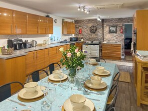A modern kitchen with wooden cabinets, a dining area set for four with a blue tablecloth, and a brick-patterned wall.