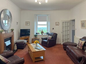 Una sala de estar con chimenea, televisión, sillón de cuero, sofá y ventana con vistas al campo.