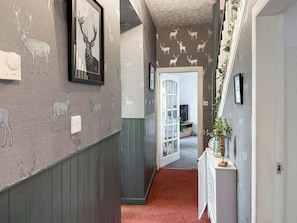 Un pasillo con papel tapiz estampado, un cuadro de un ciervo enmarco, un radiador y una puerta que da a otra habitación.