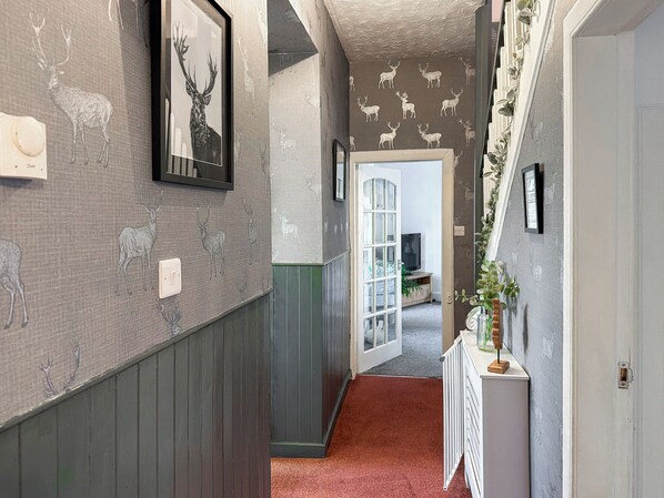 Un pasillo con papel tapiz estampado, un cuadro de un ciervo enmarco, un radiador y una puerta que da a otra habitación.