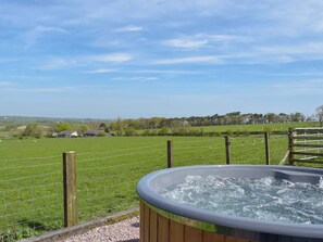 Un jacuzzi con estructura de madera, rodeado por un campo de césped y una valla de madera.